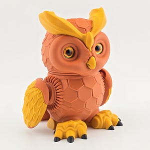 May include: A 3D-printed owl figurine in shades of orange and yellow. The owl has large, detailed eyes, a textured body, and articulated wings and feet. The design features a honeycomb pattern on the body and is set against a white background.