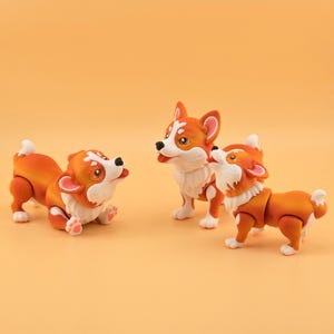 Pu&ograve; includere: Tre figurine di corgi arancioni e bianchi sono esposte su uno sfondo arancione uniforme. Una statuina &egrave; sdraiata, un'altra &egrave; in piedi e la terza guarda in alto. I corgi hanno giunture articolate.