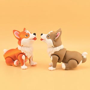 Pu&ograve; includere: Due statuette di cani corgi. Una &egrave; arancione e bianca, l'altra marrone e bianca. Entrambe hanno pelliccia bianca intorno al collo e zampe bianche. Sono posizionate l'una di fronte all'altra su uno sfondo giallo.