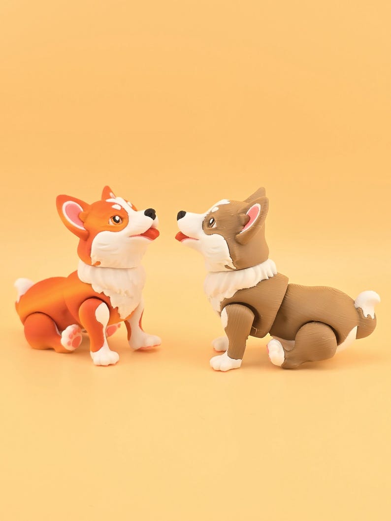 Pu&ograve; includere: Due statuette di cani corgi. Una &egrave; arancione e bianca, l'altra marrone e bianca. Entrambe hanno pelliccia bianca intorno al collo e zampe bianche. Sono posizionate l'una di fronte all'altra su uno sfondo giallo.
