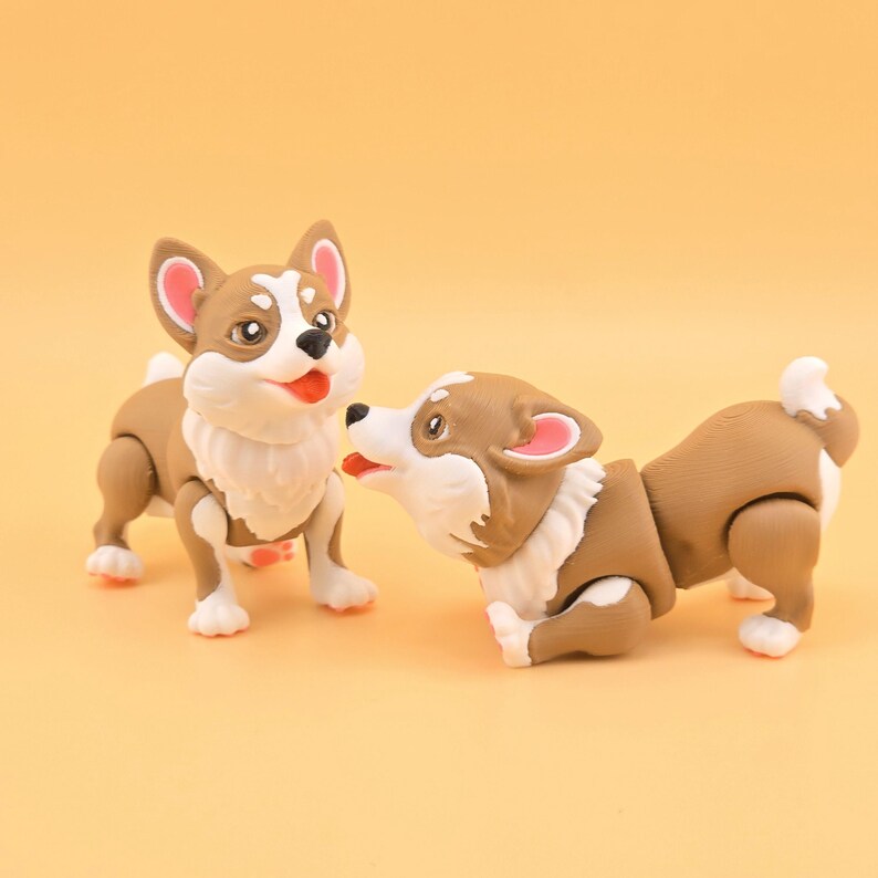 Pu&ograve; includere: Due statuette di cani corgi. Uno &egrave; in piedi, l'altro &egrave; in posa giocosa. I cani hanno pelo marrone e bianco, orecchie rosa e lingue rosse. Lo sfondo &egrave; di colore giallo pieno.