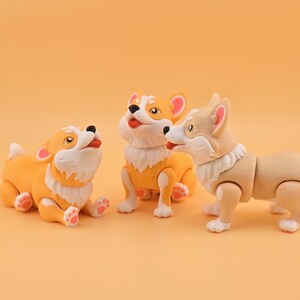 Pu&ograve; includere: Tre giocattoli di cani corgi in varie pose. I corgi sono principalmente arancioni e bianchi, con dettagli rosa sulle orecchie e sulle zampe. Hanno la pelliccia bianca intorno al collo e sono su uno sfondo arancione.