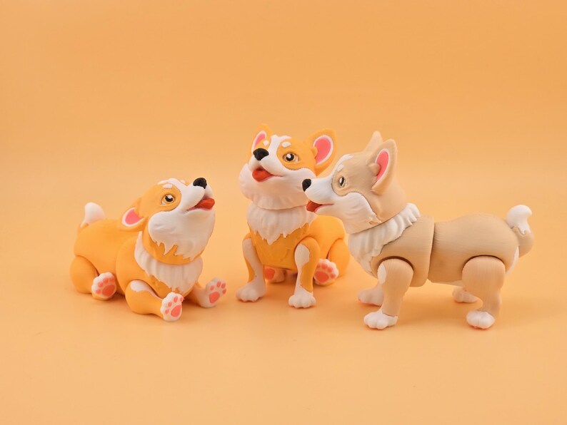 Pu&ograve; includere: Tre giocattoli di cani corgi in varie pose. I corgi sono principalmente arancioni e bianchi, con dettagli rosa sulle orecchie e sulle zampe. Hanno la pelliccia bianca intorno al collo e sono su uno sfondo arancione.