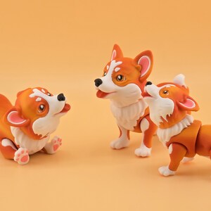 Pu&ograve; includere: Tre statuette di cani corgi arancioni e bianchi in varie pose. Uno &egrave; sdraiato, un altro &egrave; in piedi e il terzo guarda in alto. Le statuette hanno dettagli di pelliccia bianca e nasi neri, su uno sfondo arancione.