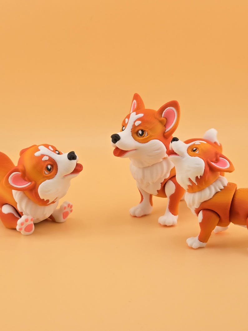 Pu&ograve; includere: Tre statuette di cani corgi arancioni e bianchi in varie pose. Uno &egrave; sdraiato, un altro &egrave; in piedi e il terzo guarda in alto. Le statuette hanno dettagli di pelliccia bianca e nasi neri, su uno sfondo arancione.