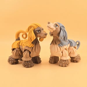 May include: Two decorative dog figurines. One dog has a yellow head and a brown body, while the other has a blue head and a tan body. Both dogs have detailed fur and are posed facing each other against a solid orange background.