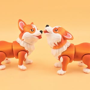 Pu&ograve; includere: Due statuette di cani corgi arancioni e bianchi. I cani sono uno di fronte all'altro, uno con la lingua di fuori. Le statuette hanno giunture articolate e pelliccia bianca intorno al collo e sulle zampe.