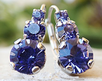 May include: A pair of silver earrings with three purple crystal stones. The earrings have a hoop design.