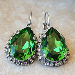 May include: A pair of dangle earrings with a large pear-shaped green gemstone surrounded by a halo of smaller clear rhinestones.