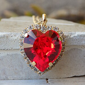 May include: A gold heart-shaped pendant necklace with a large red crystal in the centre and a border of smaller clear crystals.