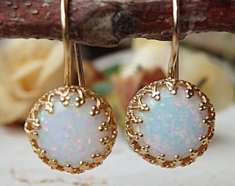 Könnte beinhalten: Ein Paar goldene Ohrringe mit weißen Opal-Steinen, die in einem filigranen Design gefasst sind.