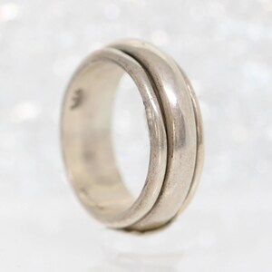 May include: A silver ring with a wide band that is made of two overlapping pieces.