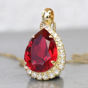 Puede incluir: Un collar de oro con un colgante de gran piedra roja en forma de lágrima rodeada por un halo de piedras transparentes más pequeñas.
