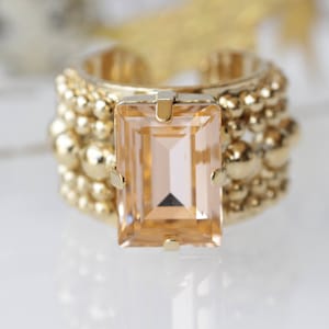 May include: A gold ring with a large, rectangular, light brown gemstone. The ring is made of small, round beads.