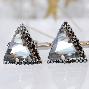 Puede incluir: Un par de gemelos de plata con un cristal transparente triangular engastado en un bisel negro.
