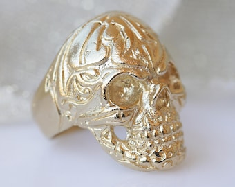 May include: A gold skull ring with intricate details and a textured surface.