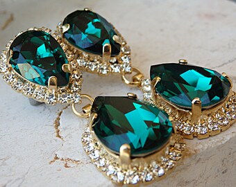 May include: A pair of emerald green teardrop earrings with gold settings and a halo of clear rhinestones.