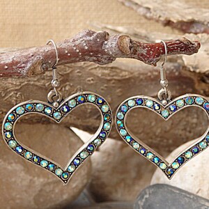 Pu&ograve; includere: Un paio di orecchini a forma di cuore argentati con strass blu e verdi iridescenti.