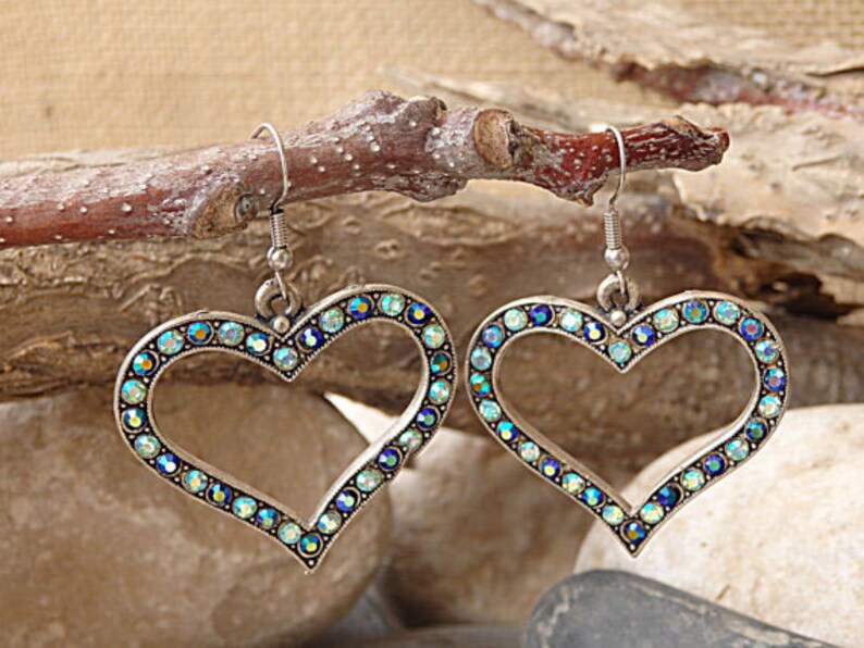 Pu&ograve; includere: Un paio di orecchini a forma di cuore argentati con strass blu e verdi iridescenti.