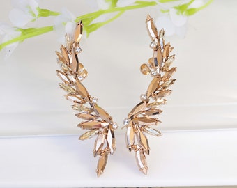 May include: A pair of gold ear cuffs with clear and amber crystals arranged in a wing-like design.