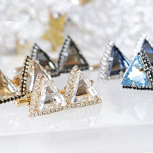 Puede incluir: Un juego de seis gemelos triangulares con bordes negros y detalles de cristal. Los gemelos est&aacute;n en tres colores: transparente, gris y azul.