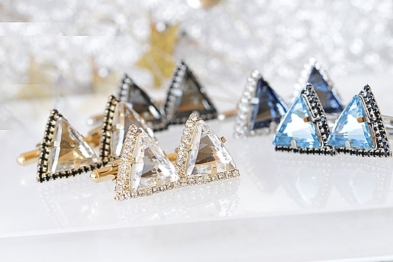 Puede incluir: Un juego de seis gemelos triangulares con bordes negros y detalles de cristal. Los gemelos est&aacute;n en tres colores: transparente, gris y azul.