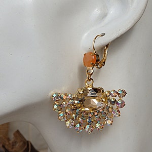 May include: Gold dangle earrings with a large iridescent crystal and a smaller peach-colored stone. The earrings have a hook closure.