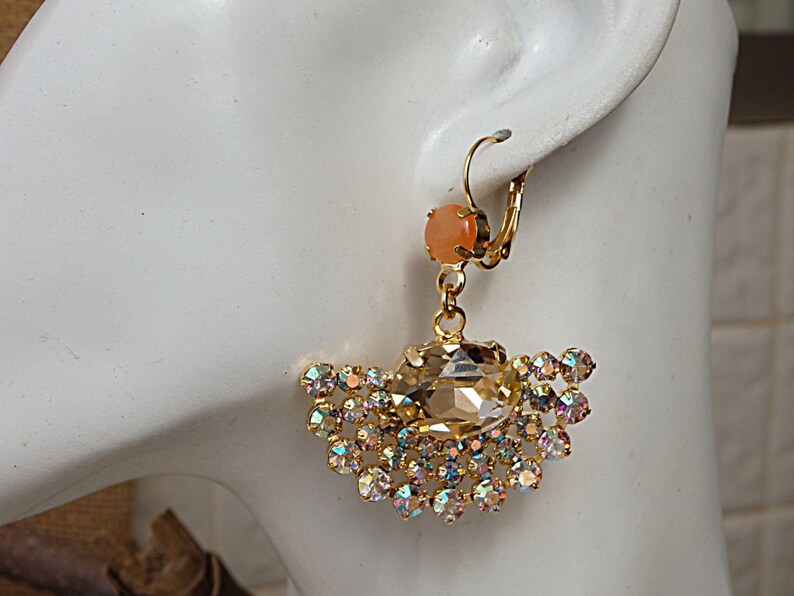 May include: Gold dangle earrings with a large iridescent crystal and a smaller peach-colored stone. The earrings have a hook closure.