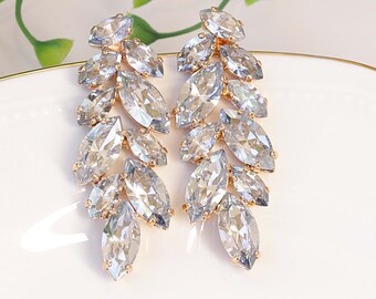 May include: A pair of elegant, leaf-shaped earrings. Each earring features multiple clear, marquise-cut crystals set in a gold-tone metal. The crystals cascade downward, creating a sparkling, eye-catching design. The earrings are displayed on a white surface.