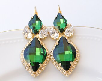 May include: A pair of emerald green and gold tone dangle earrings with clear crystal accents. The earrings feature a large emerald green teardrop-shaped stone surrounded by smaller clear crystals.