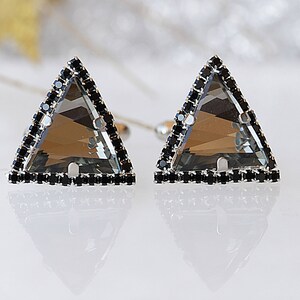Puede incluir: Un par de pendientes de forma triangular con una piedra preciosa gris transparente engastada en un marco de plata. El marco est&aacute; acentuado con una fila de piedras preciosas negras.