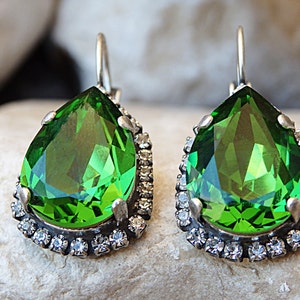 May include: A pair of dangle earrings with a large pear-shaped green gemstone surrounded by a halo of smaller clear rhinestones.
