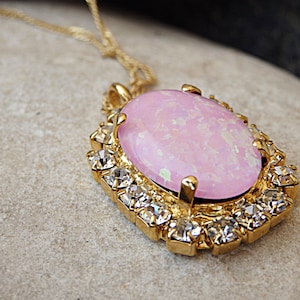 Pu&ograve; includere: Una collana d'oro con un grande ciondolo ovale in opale rosa circondato da strass trasparenti.