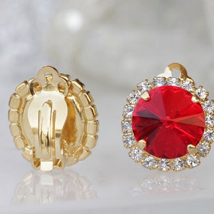 以下が含まれることがあります： 赤いラインストーンの中心に、小さなクリアなラインストーンのハローで囲まれた、ゴールドのクリップ式イヤリングのペアです。