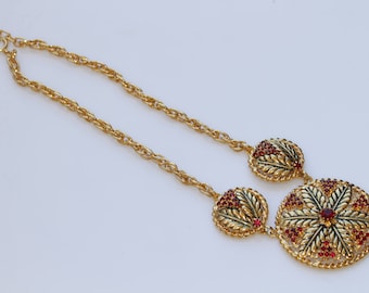 Puede incluir: Un collar de cadena dorada con tres colgantes de color rojo y dorado. Los colgantes tienen forma de hojas y un diseño floral.