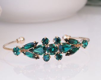 May include: A gold bangle bracelet with a cluster of emerald green rhinestones in a leaf-like design.