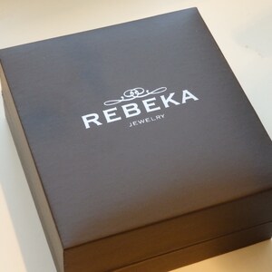 May include: A dark brown rectangular box with the text "REBEKA JEWELRY" in white lettering.