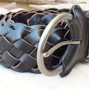 May include: A black leather braided belt with a silver buckle. The belt is woven in a basket weave pattern.