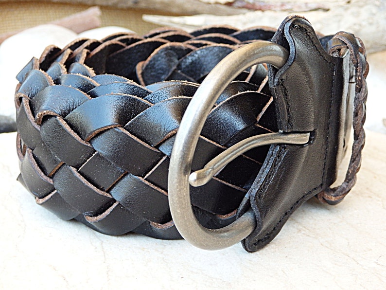 May include: A black leather braided belt with a silver buckle. The belt is woven in a basket weave pattern.