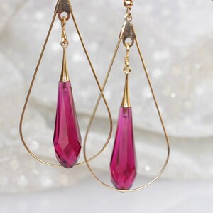 May include: A pair of gold teardrop earrings with dangling fuchsia crystal drops.