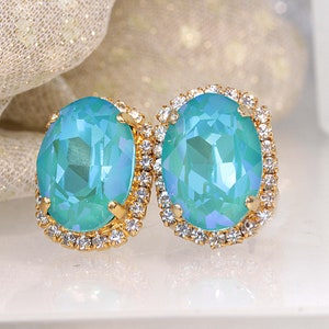 Puede incluir: Un par de pendientes ovalados con una piedra preciosa azul claro rodeada por un halo de brillantes transparentes. Los pendientes tienen un engaste de oro.