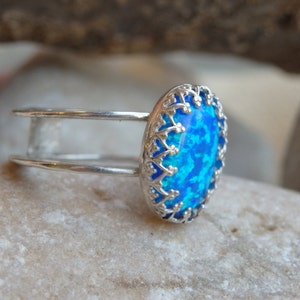 May include: A silver ring featuring a blue opal stone set within an ornate filigree design.
