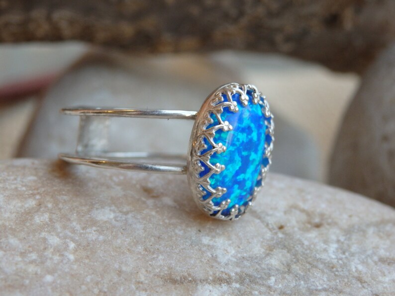 May include: A silver ring featuring a blue opal stone set within an ornate filigree design.