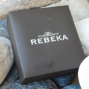 May include: A black box with the word "REBEKA" printed in white on the top. The box is surrounded by rocks.