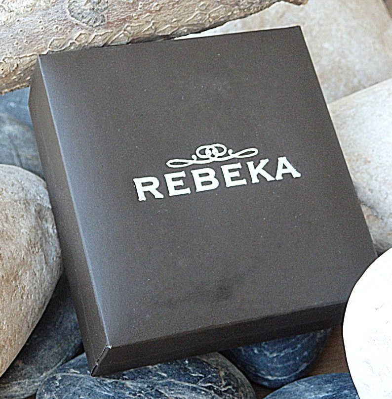 May include: A black box with the word "REBEKA" printed in white on the top. The box is surrounded by rocks.