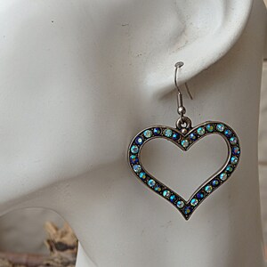 Pu&ograve; includere: Orecchini pendenti a forma di cuore in argento con un bordo di cristalli iridescenti blu e verdi.