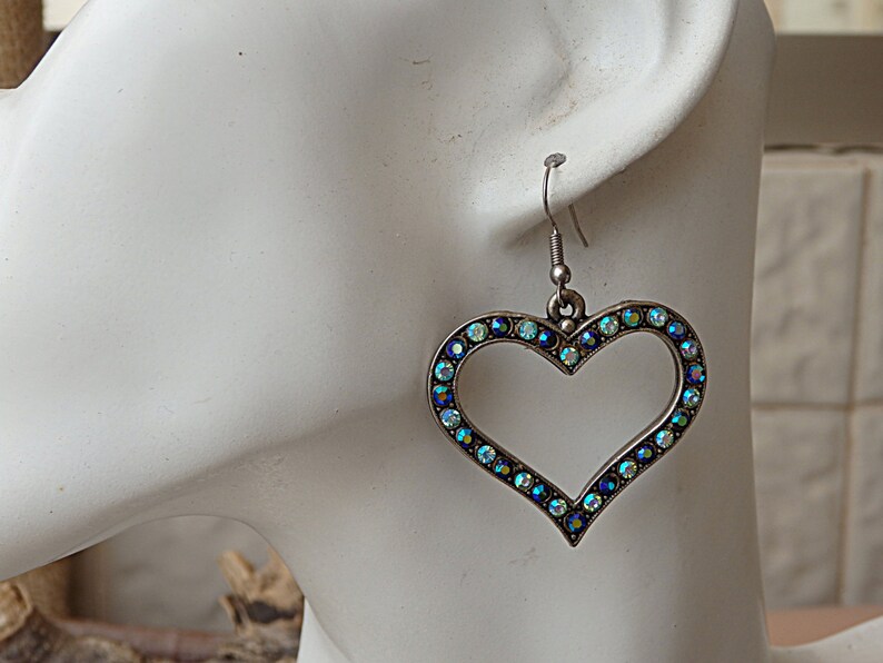 Pu&ograve; includere: Orecchini pendenti a forma di cuore in argento con un bordo di cristalli iridescenti blu e verdi.