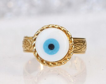May include: Gold ring with a white oval-shaped stone featuring a blue evil eye design.