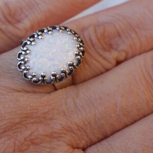 May include: A silver ring with an oval-shaped white opal stone set in a decorative filigree design.