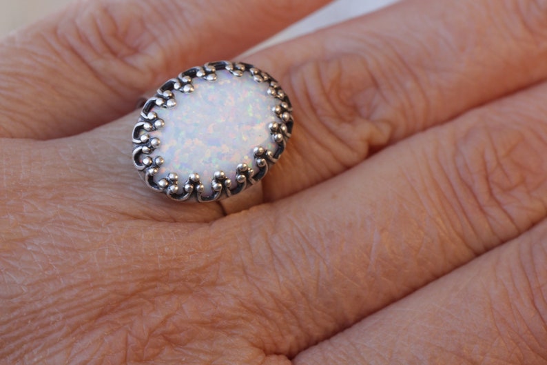 May include: A silver ring with an oval-shaped white opal stone set in a decorative filigree design.